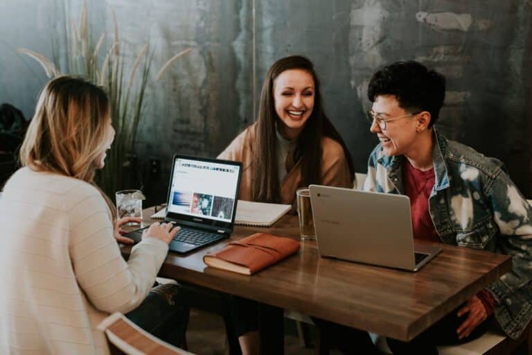 A man and two women with laptops laughing at work.