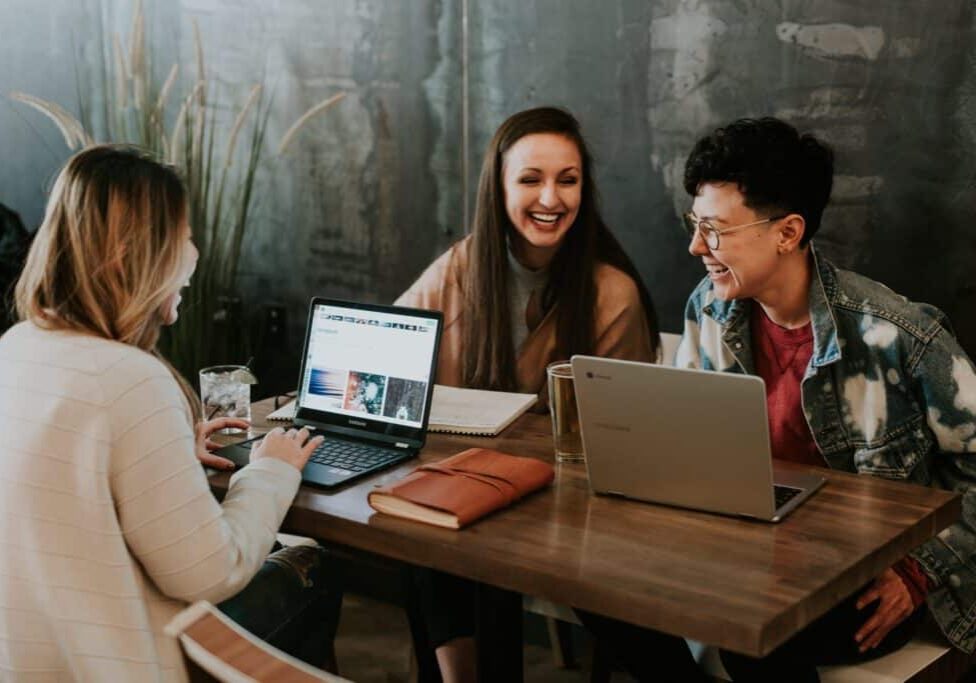 3 women sitting at a table with their laptops working
