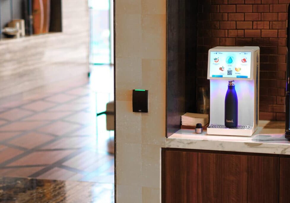 Bevi countertop water dispenser in office kitchen with a man and woman holding beverages and talking to each other