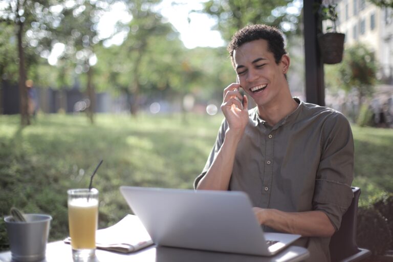 Man sitting outside at a table on the phone with his laptop