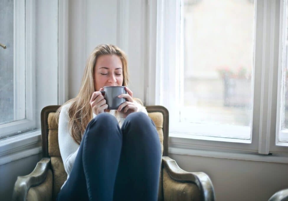 woman sitting in a chair with her knees to her chest, drinking a cup of coffee