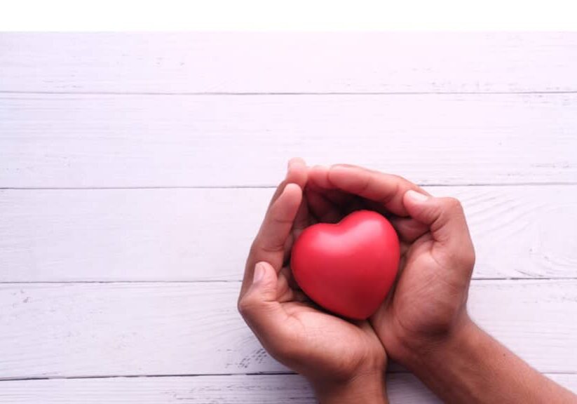 Two hands cupping a heart-shaped red fruit