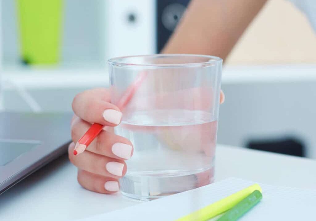 Woman's hand holding a glass of water on a desk