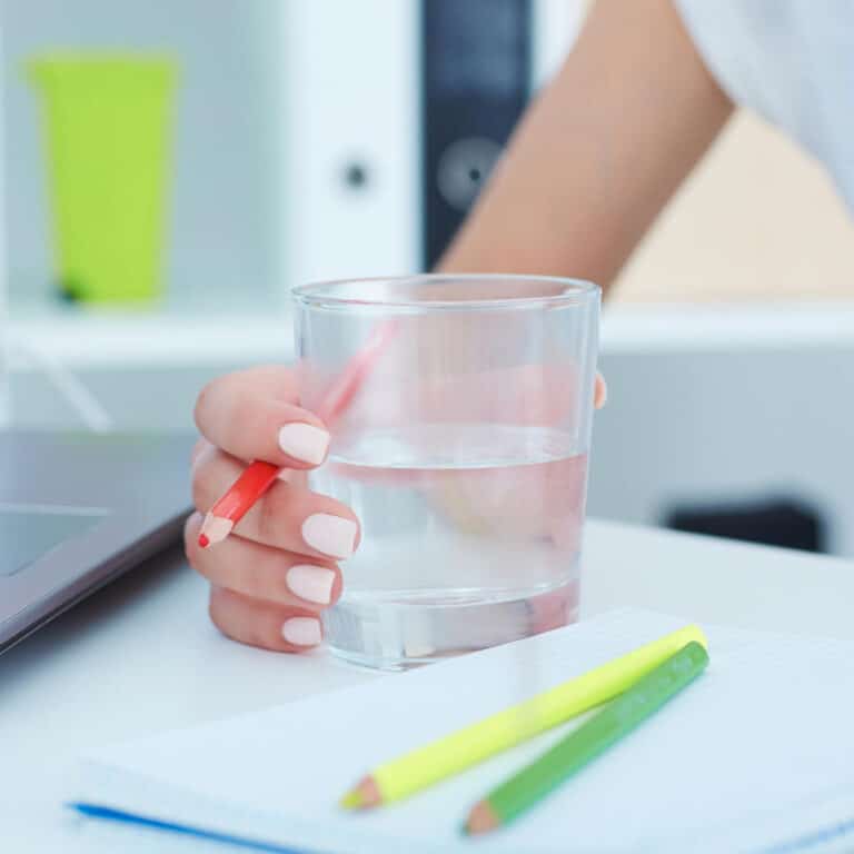 Woman's hand holding a glass of water on a desk