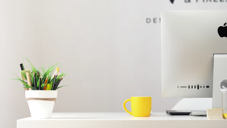 small plant in a white flower pot and single yellow coffee mug on a white counter